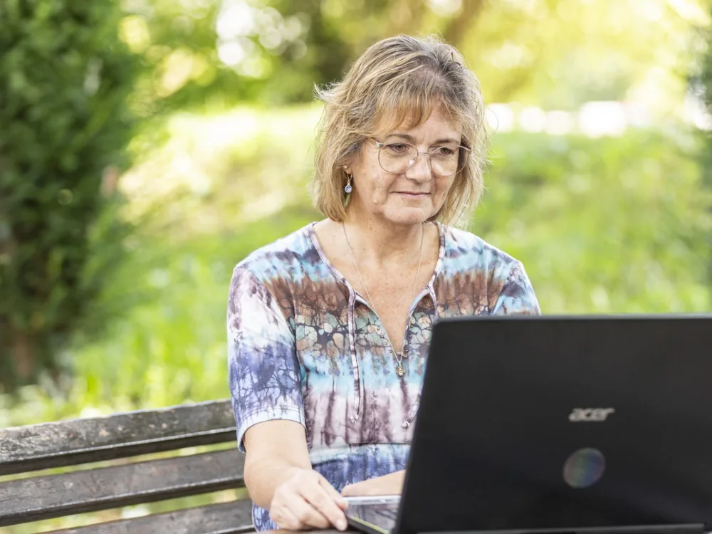 Monika Rudolph arbeitet mit dem Laptop auf einer Parkbank im Grünen